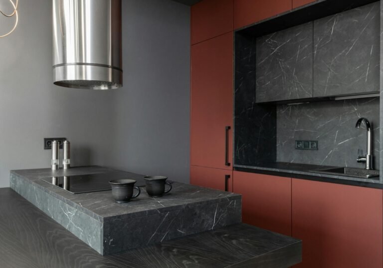 Modern kitchen with dark marble countertops, red cabinets, and a stainless steel range hood.